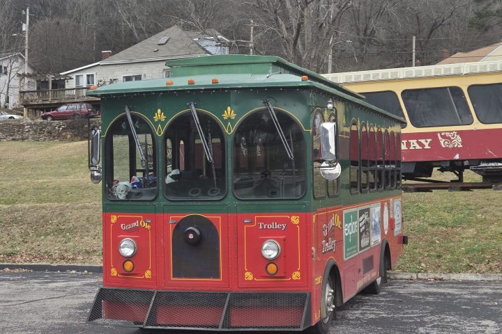Colorful trolley parked in a lot with bare trees and hills in the background.