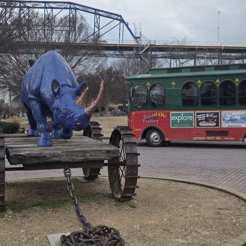 Blue rhino sculpture on a wagon near a green and red trolley bus.