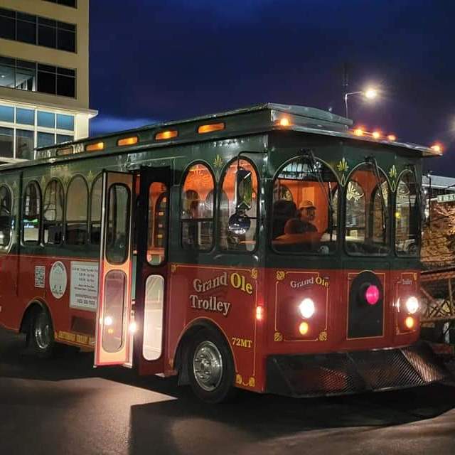Traditional red trolley parked at night with lit building and street lights in the background.