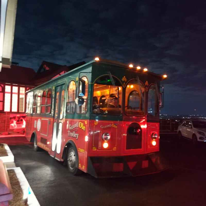Red and green trolley labeled 'Grand Ole' on a dark road at night.