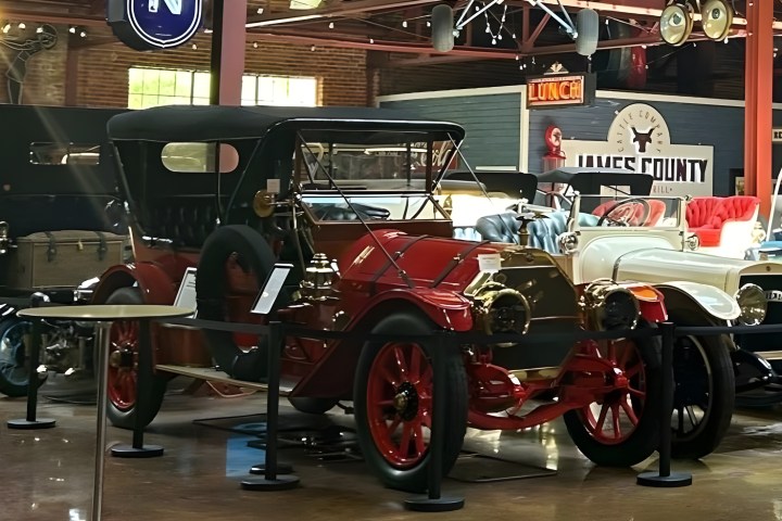 Vintage cars displayed in a museum setting with signs and lights above.