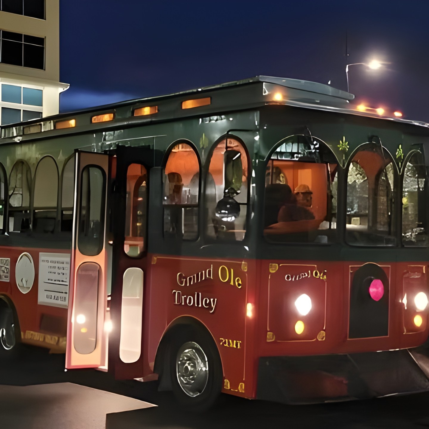 Red trolley parked near a building at night with lights on.